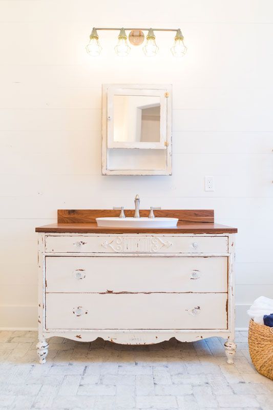 White farmhouse bathroom vanity with mirror, sink, and wall light in a bright room