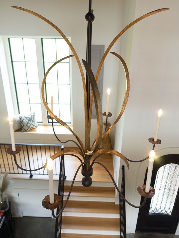 Grand staircase with ornate chandelier, curved antler-like arms, and tall windows in a bright foyer