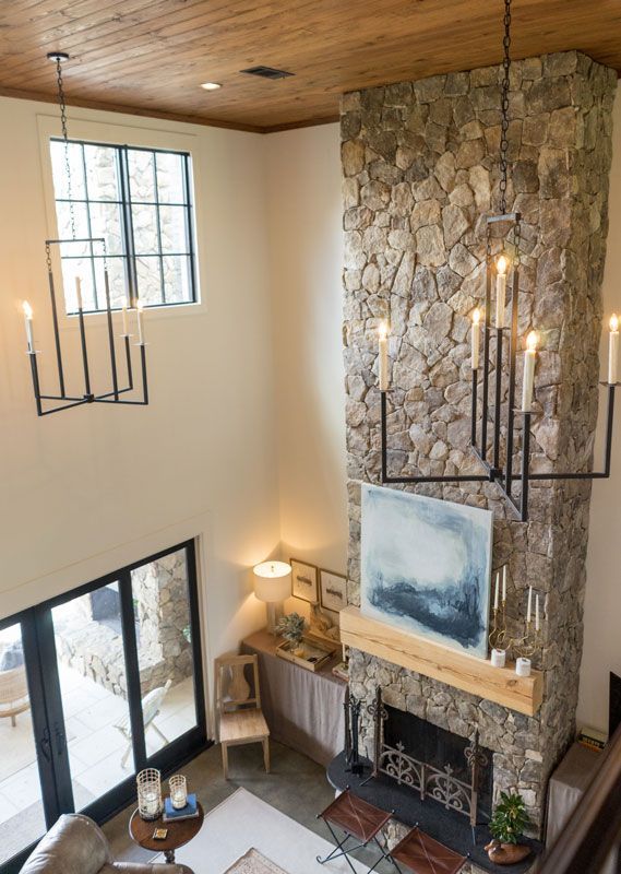 Modern living room with tall stone fireplace, large window, wood ceiling, and black pendant lights