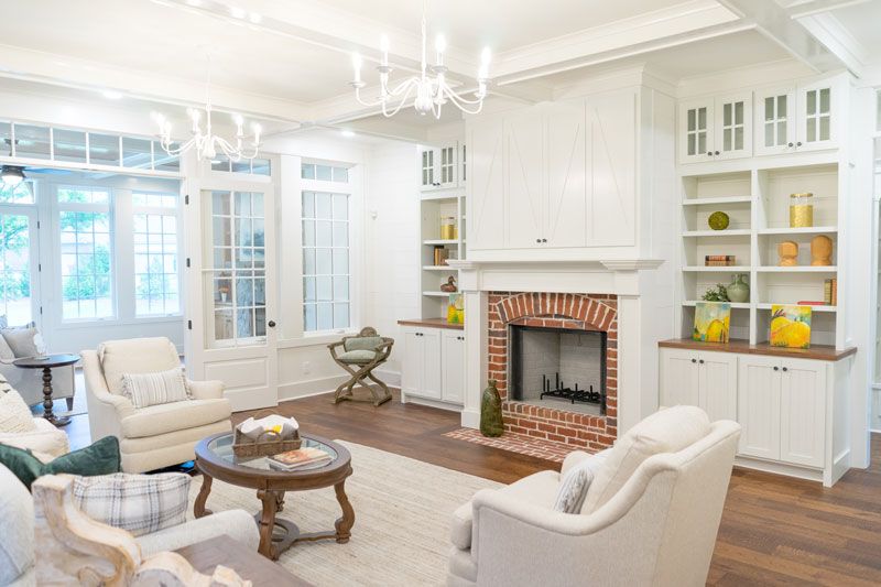 Bright white living room with fireplace, built-in shelves, cream chairs, and a round wooden coffee table