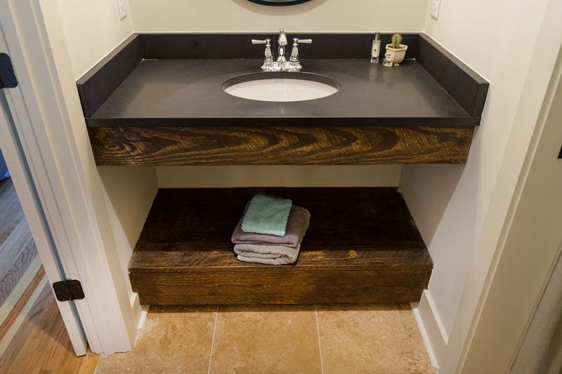 Small bathroom vanity with sink, black countertop, wood cabinet, and folded towels on the lower shelf.