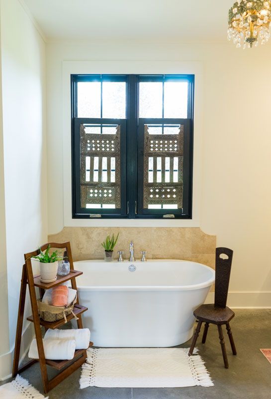 Modern bathroom with freestanding tub, window, wooden ladder shelf, and chair on a beige wall.