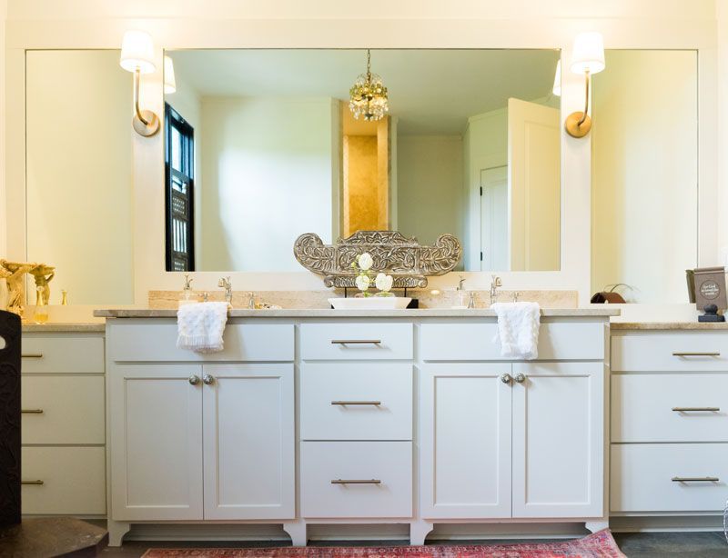 Bright bathroom vanity with double sinks, white cabinets, mirrors, and wall sconces