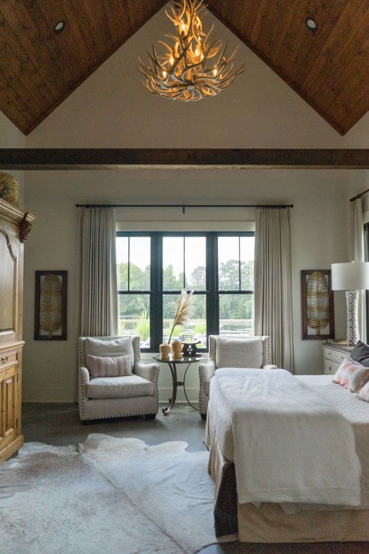 Elegant bedroom with vaulted wood ceiling, chandelier, large window, and white bedding