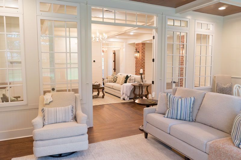 Bright, elegant living room with white trim, light gray sofas, and a view into a cozy sitting area