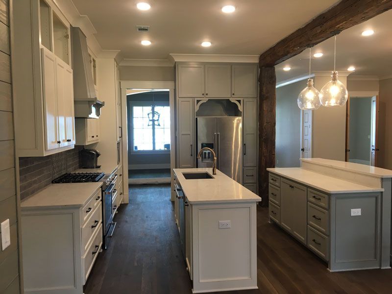 Bright modern kitchen with white cabinets, central island, pendant lights, and dark wood floor