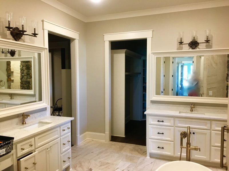 Bright bathroom with double vanities, large mirrors, and an open doorway to a dark walk-in closet