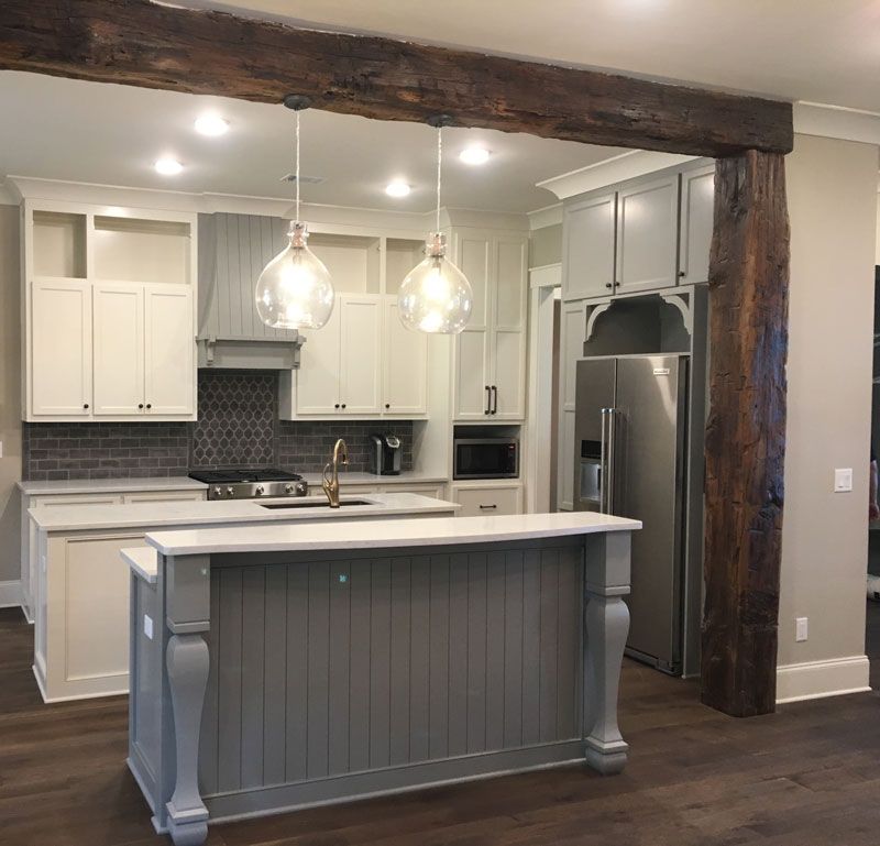Modern kitchen with gray island, white cabinets, stainless appliances, and exposed wood beam