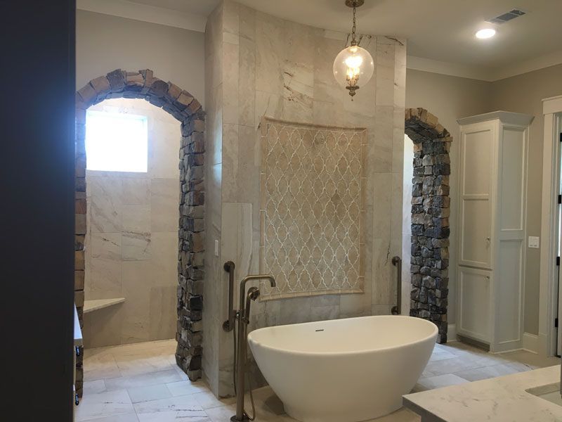 Luxury bathroom with freestanding tub, arched stone doorways, and tiled shower area