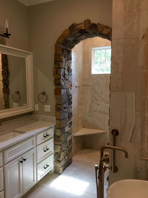 Bathroom with stone-arched shower, beige tile, white vanity, and bright window light
