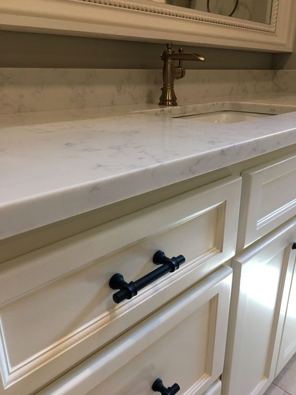 White bathroom vanity with marble countertop, black drawer pulls, and chrome faucet beneath a mirror