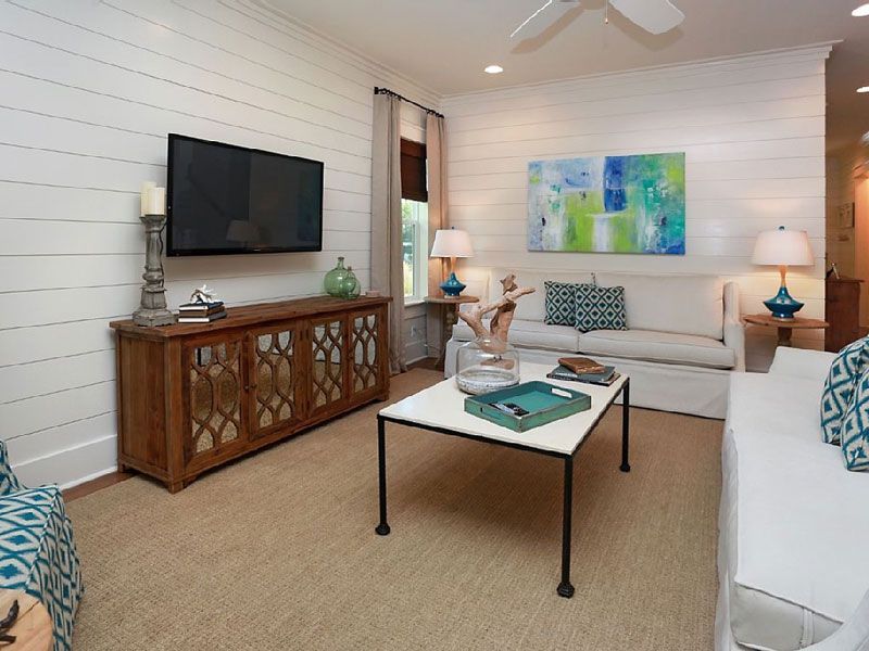 Bright living room with white sofa, TV, wooden cabinet, and coffee table with teal accents.