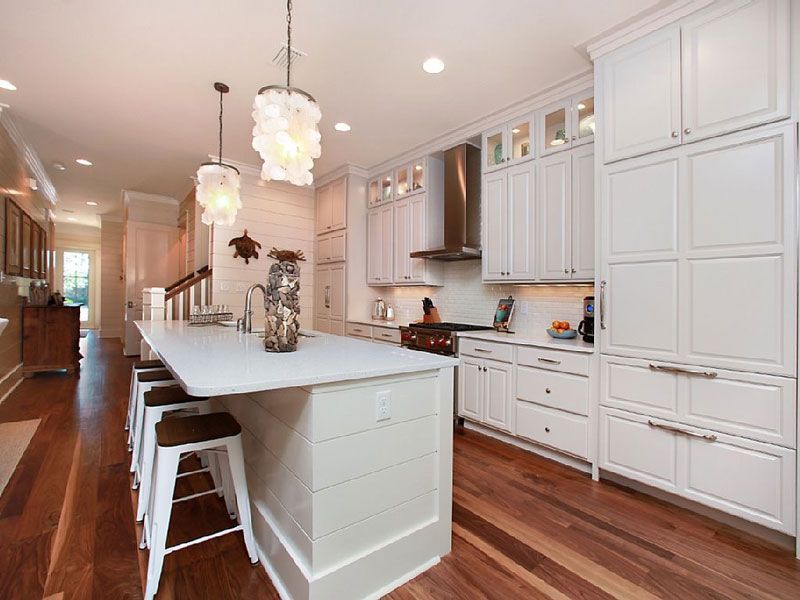 Bright modern kitchen with white cabinets, marble island, pendant lights, and hardwood floors.