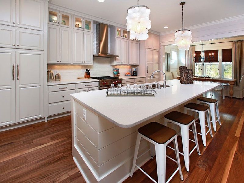 Modern white kitchen with a large island, bar stools, and hardwood floors