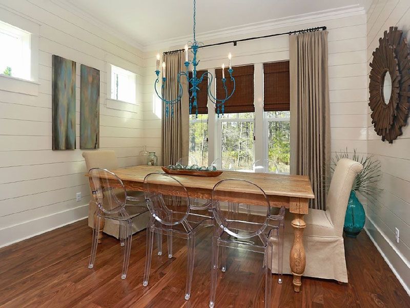 Bright dining room with a wooden table, clear chairs, wall art, and windows with blinds