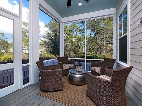 Covered porch with wicker chairs, a small table, and wooded views beyond the railing.