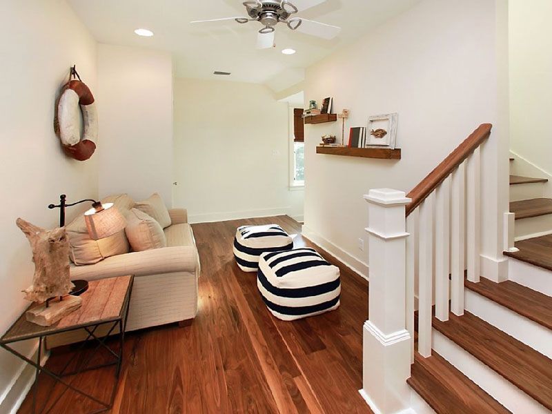 Bright white living room with wood floors, beige sofa, striped ottomans, and staircase railing.