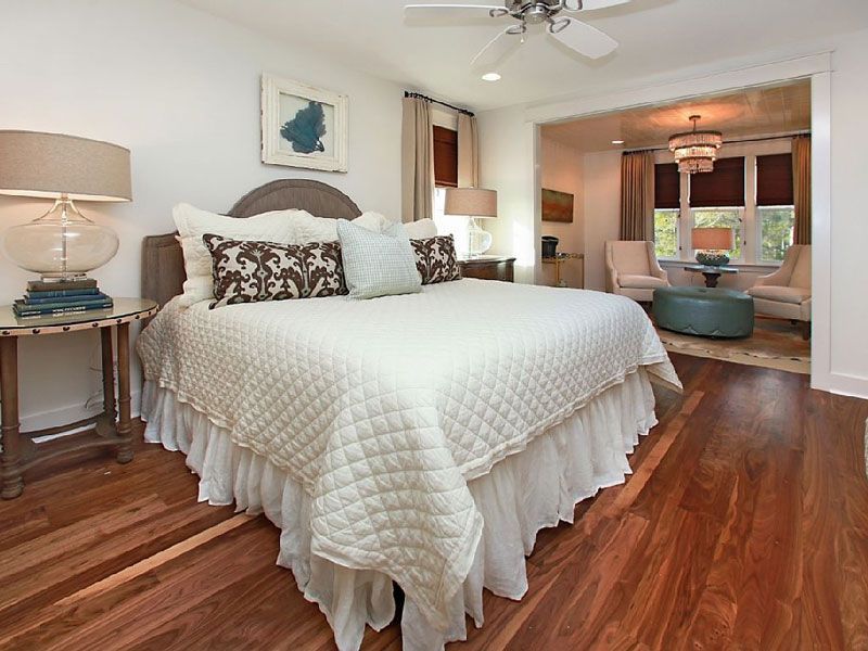 Bright bedroom with a white quilted bed, wood floors, and a cozy sitting area in the background
