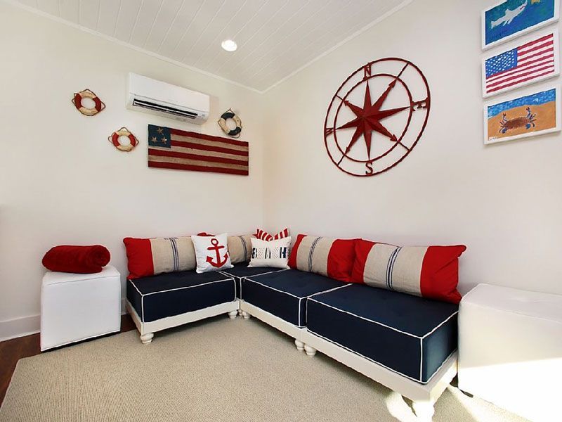 Nautical-themed living room with navy sectional, red-white pillows, wall decor, and U.S. flag art