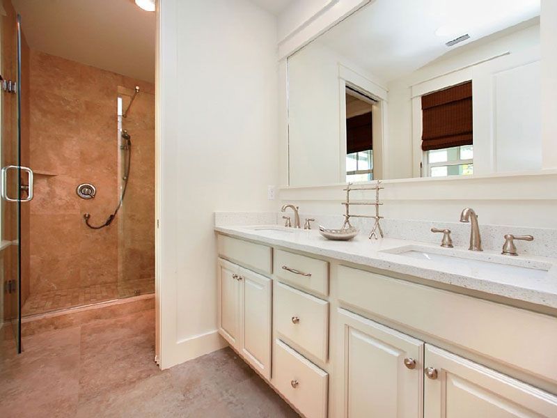 Bathroom with white vanity and mirror beside a glass shower with tan tile