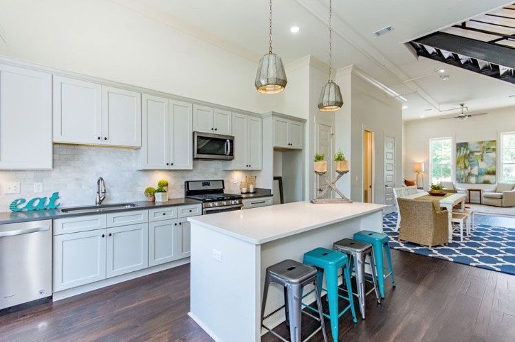 Bright modern kitchen with white cabinets, island seating, and blue accents leading into a living area