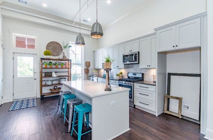 Bright modern kitchen with white cabinets, island, teal stools, and dark wood floors