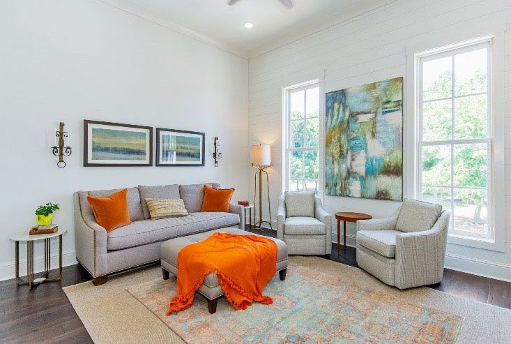 Bright living room with gray sofas, orange accents, framed art, and large windows