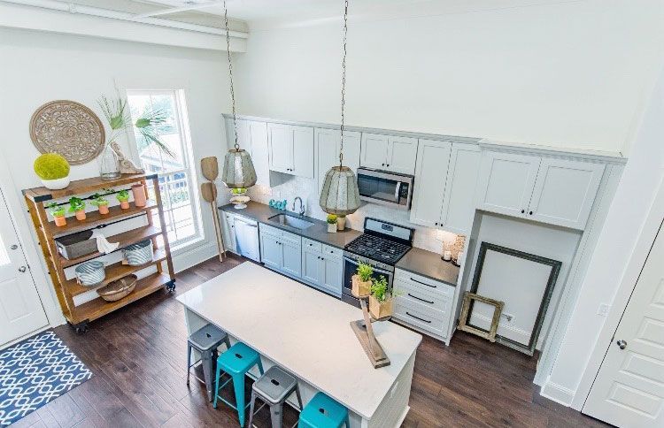 Bright modern kitchen with island, blue stools, white cabinets, and wood floors, viewed from above