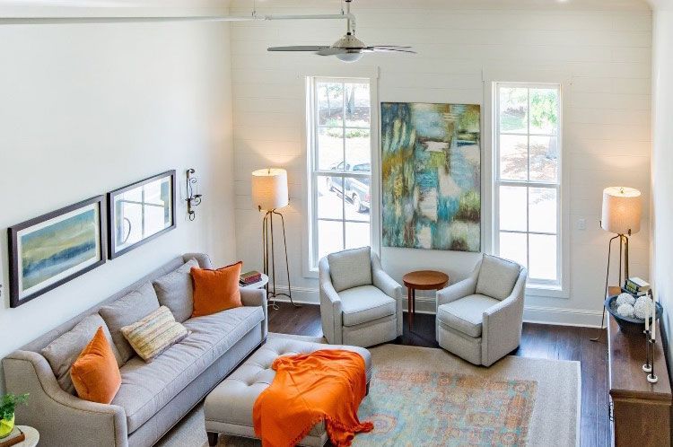 Bright living room with gray sofa, two armchairs, orange accents, and large abstract wall art