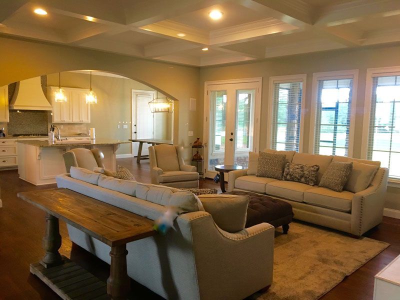 Bright open living room with beige sofas, armchairs, wooden table, and kitchen in the background