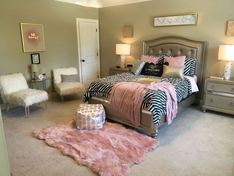 Cozy beige bedroom with tufted bed, pink rug, zebra accents, and two white chairs by the window