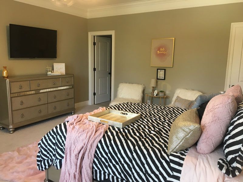 Bedroom with a striped bedspread, wall-mounted TV, dresser, and pale pink accents
