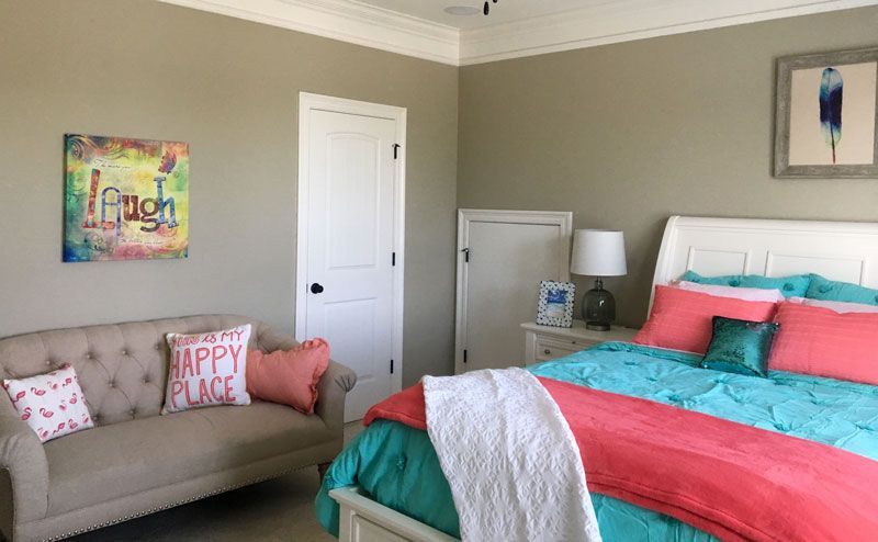 Bedroom with teal-and-coral bedspread, beige sofa, and wall art in a neutral-toned room