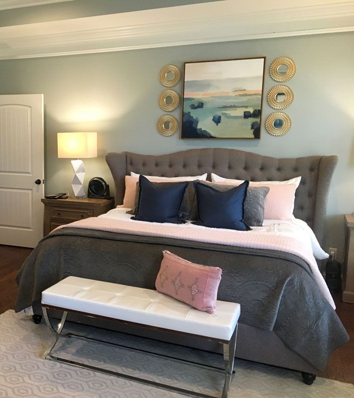 Elegant bedroom with tufted gray bed, navy pillows, bench, lamp, and framed artwork above the headboard