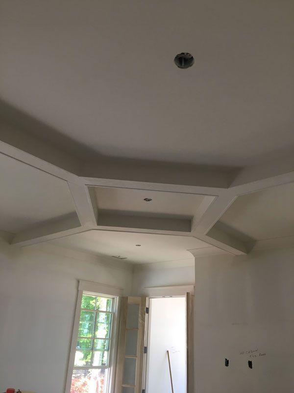 Empty room with white walls and a decorative tray ceiling, lit by a window and open door.
