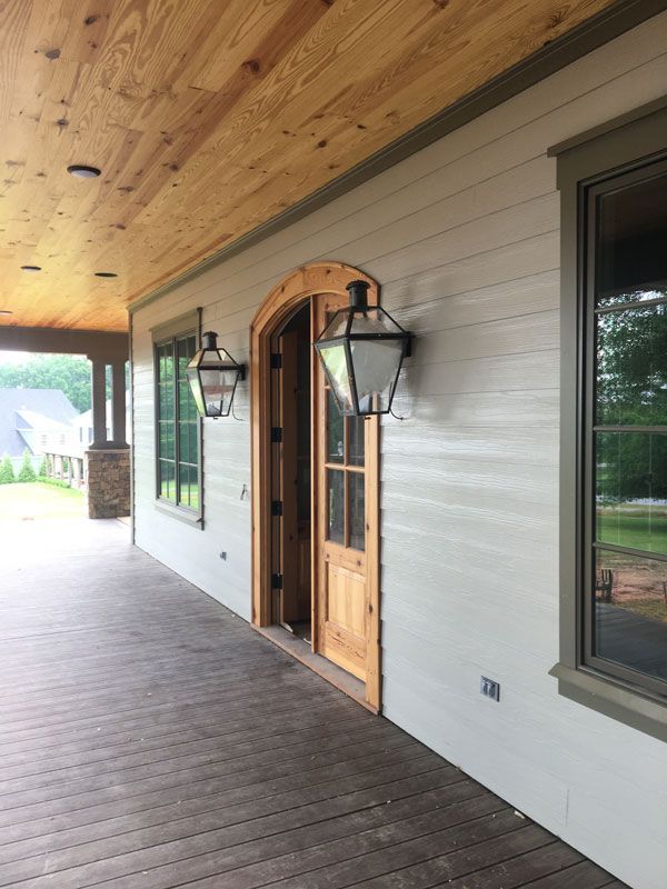 Covered porch with wood ceiling, gray siding, black lanterns, and a wooden front door.