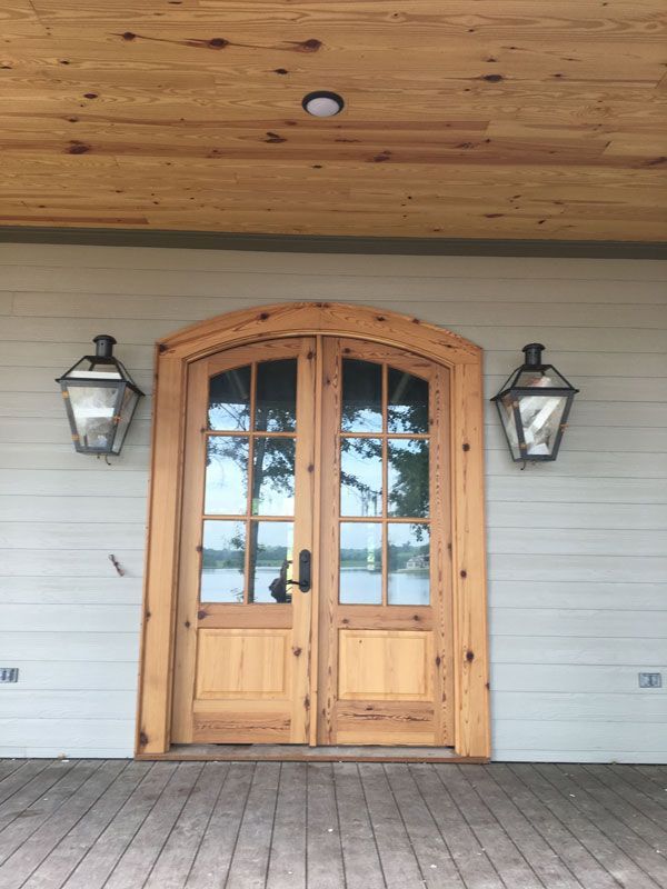 Wooden front door with arched glass panes, flanked by two black lanterns on a porch.
