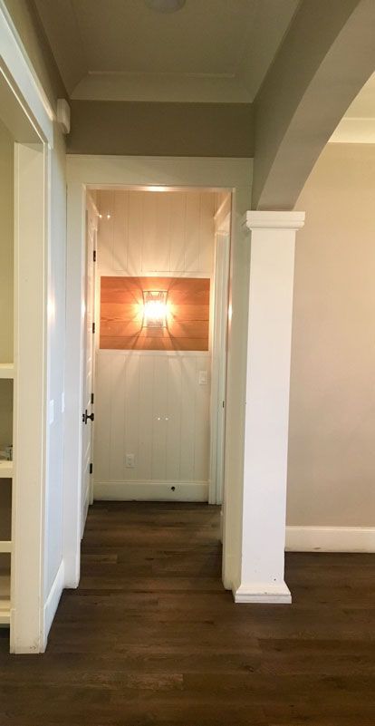 Empty hallway with dark wood floors, white columns, and a bright ceiling light at the far end.