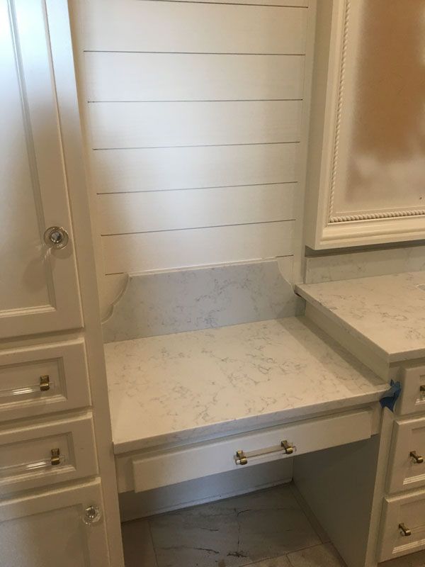 Built-in vanity desk with drawers and countertop, in a light-colored bathroom or dressing area.