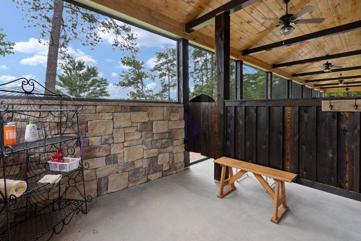 Covered patio with stone half wall, dark wood fence, and a wooden bench under a wood ceiling with fans