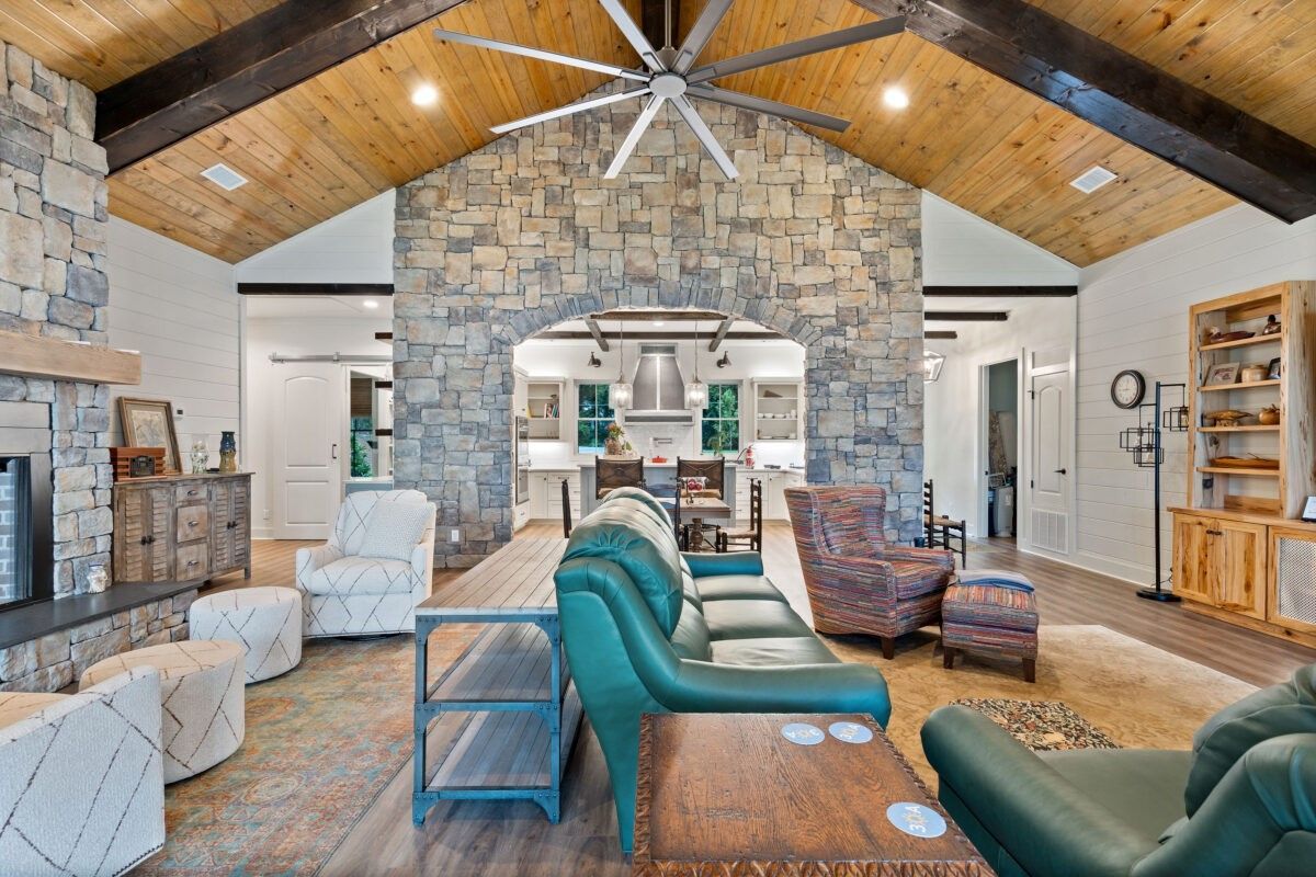 Rustic living room with stone fireplace, vaulted wood ceiling, and teal sofas around a rug