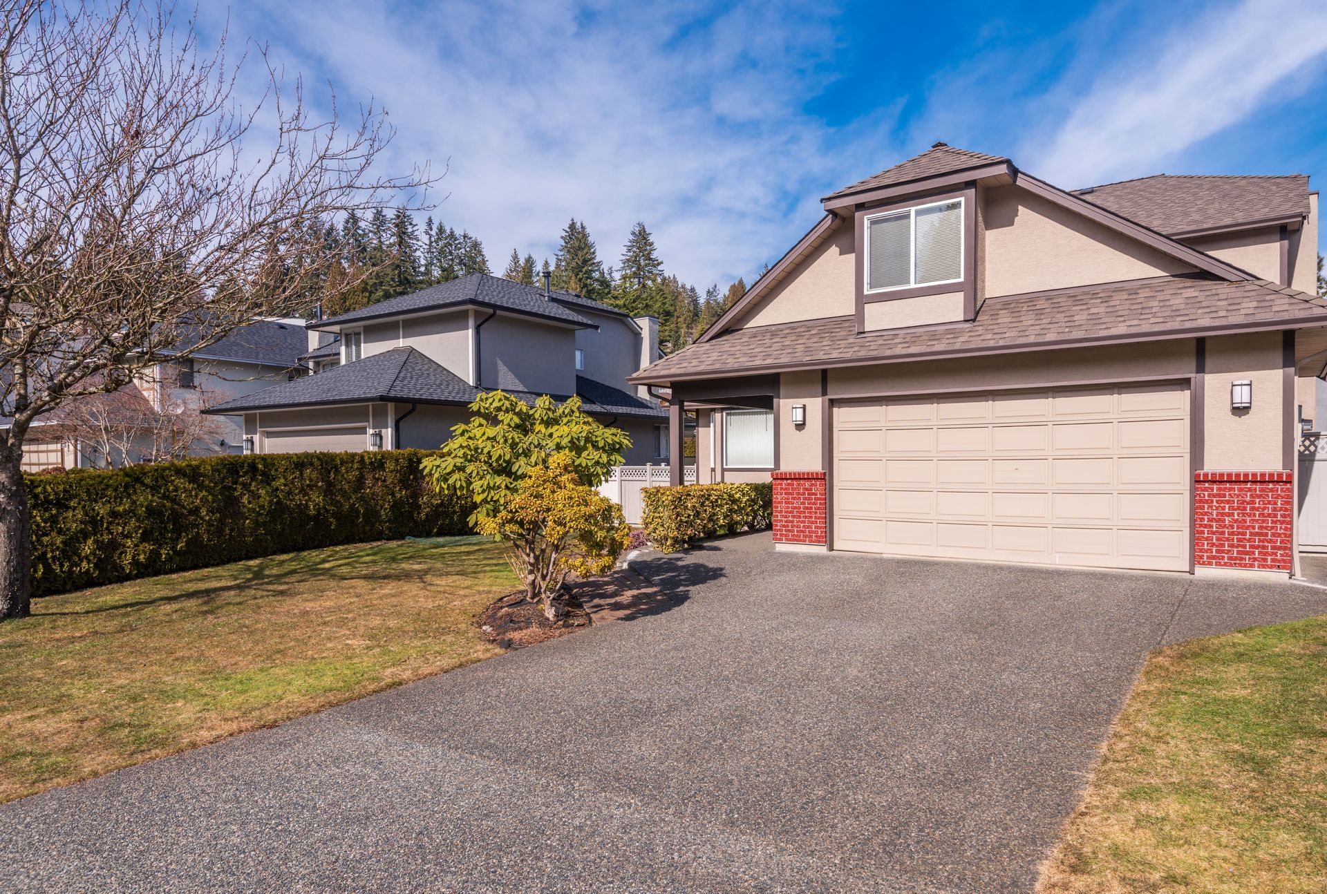 Suburban house with beige garage, paved driveway, and blue sky on a sunny day