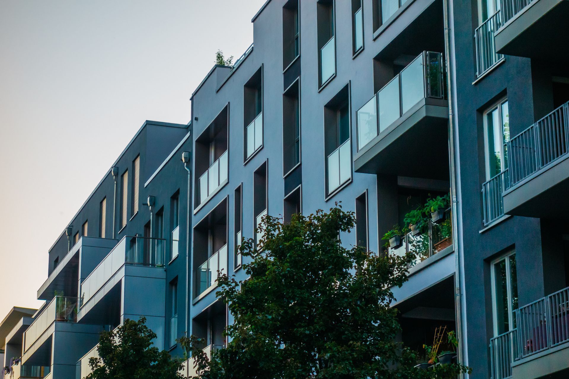 Modern apartment buildings with balconies and trees against a pale sky
