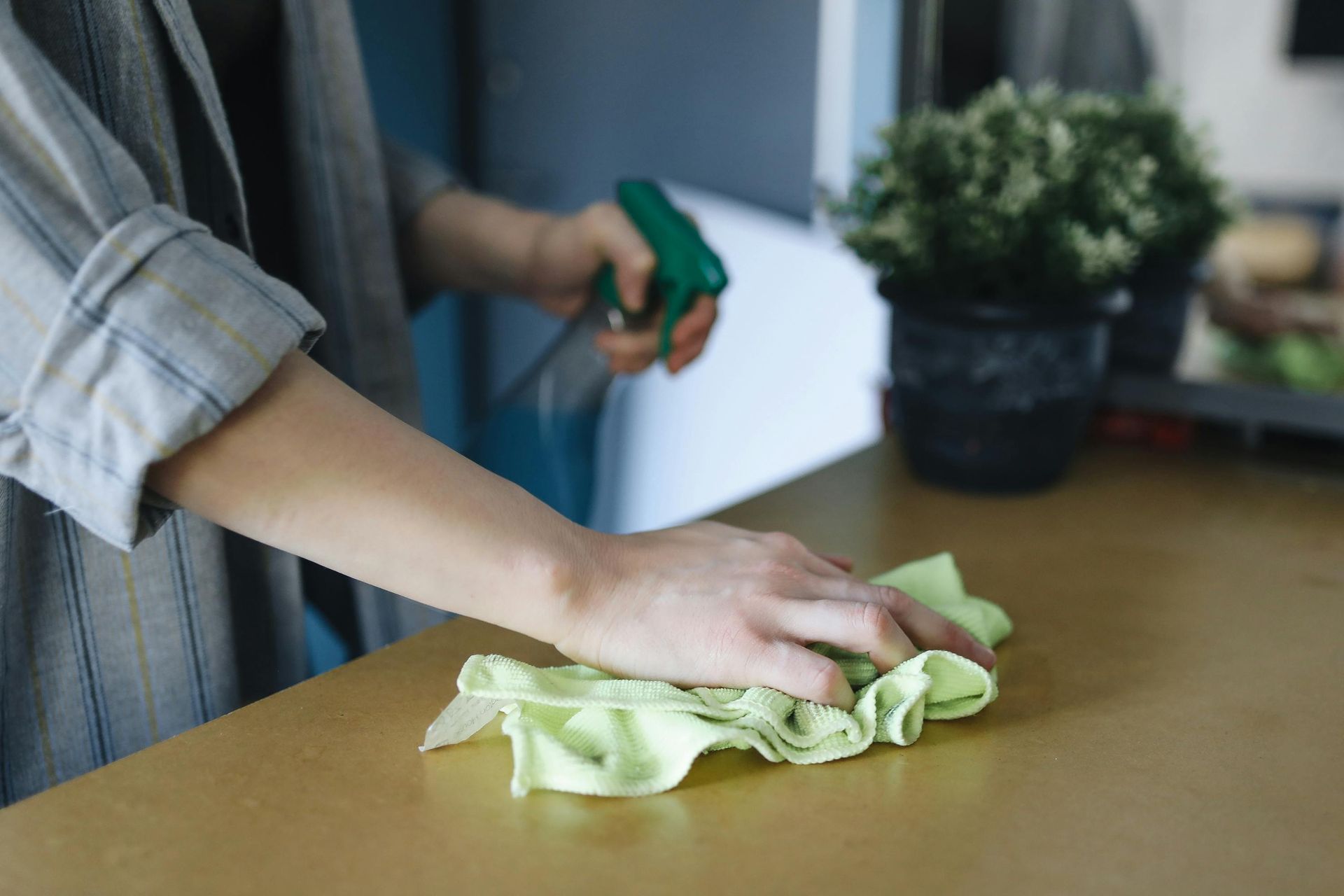 Person cleaning a wooden surface with a spray bottle and green cloth.