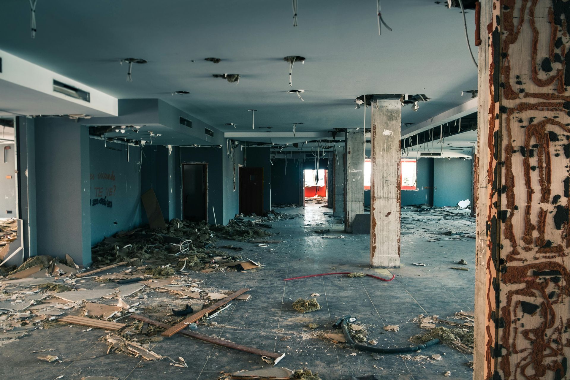 Interior view of a demolished room with debris, exposed beams, and torn walls.