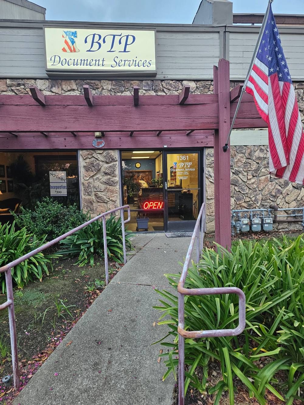 Storefront with a ramp entrance, purple awning, and American flag hanging beside the doorway