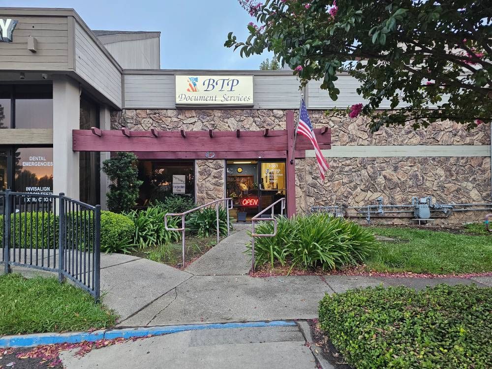 Entrance to a stone building with an American flag, maroon awning, and walkway surrounded by greenery