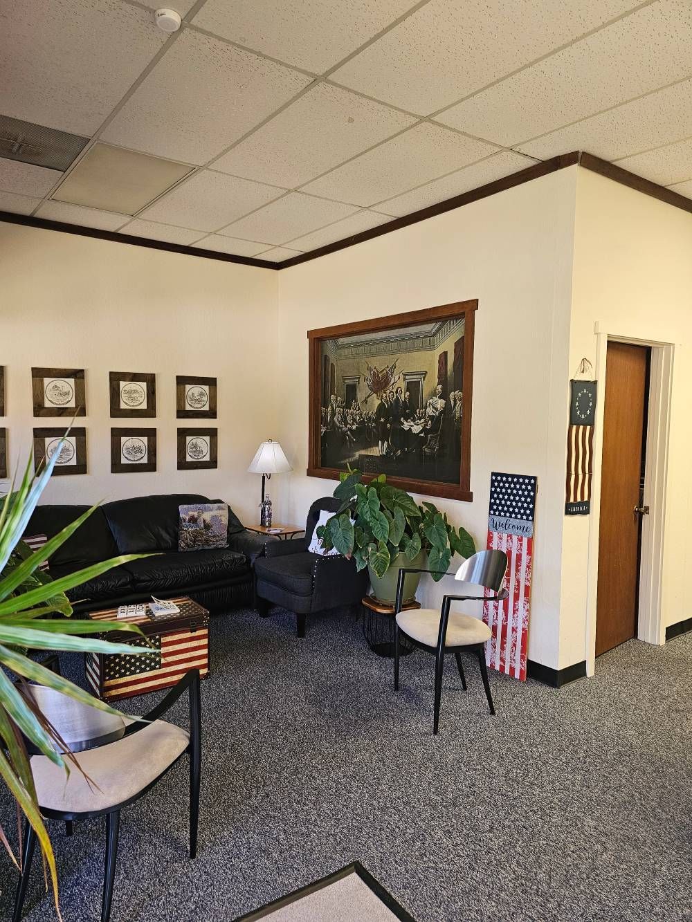 Office waiting room with black couch, framed wall art, lamp, plant, and open doorway.