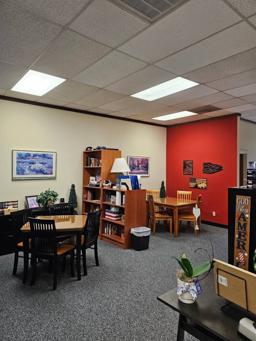 Small office lounge with tables, bookshelves, chairs, and a bright red accent wall.
