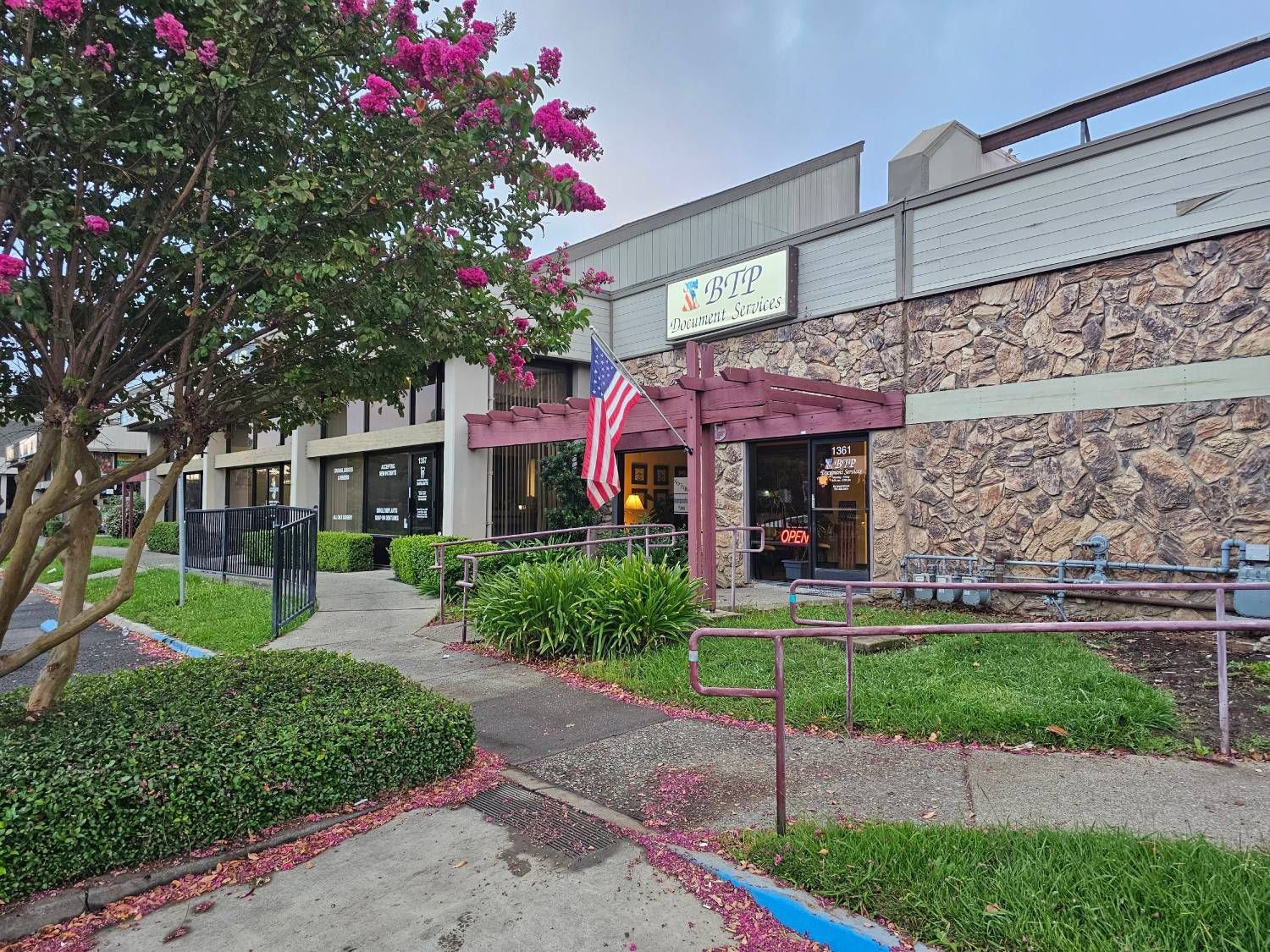 Storefront with pink awning, stone facade, and landscaped walkway under a flowering tree
